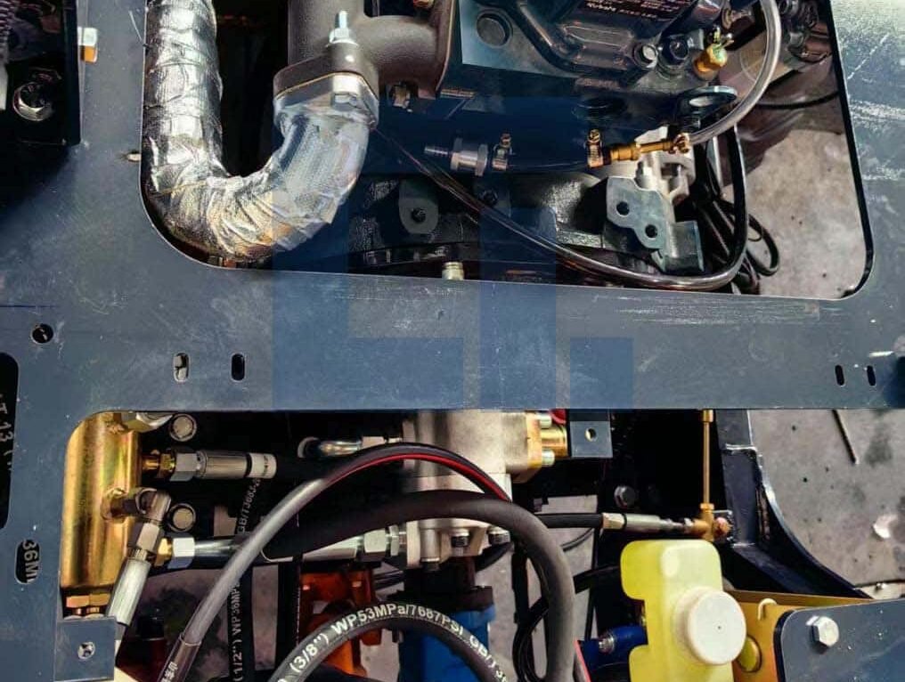 Close-up of HIGHLAND HEAVY MACHINERY HILT 50 backhoe loader optional hydraulic drive system, showing engine compartment, transmission lines, and fluid reservoir for enhanced operational efficiency