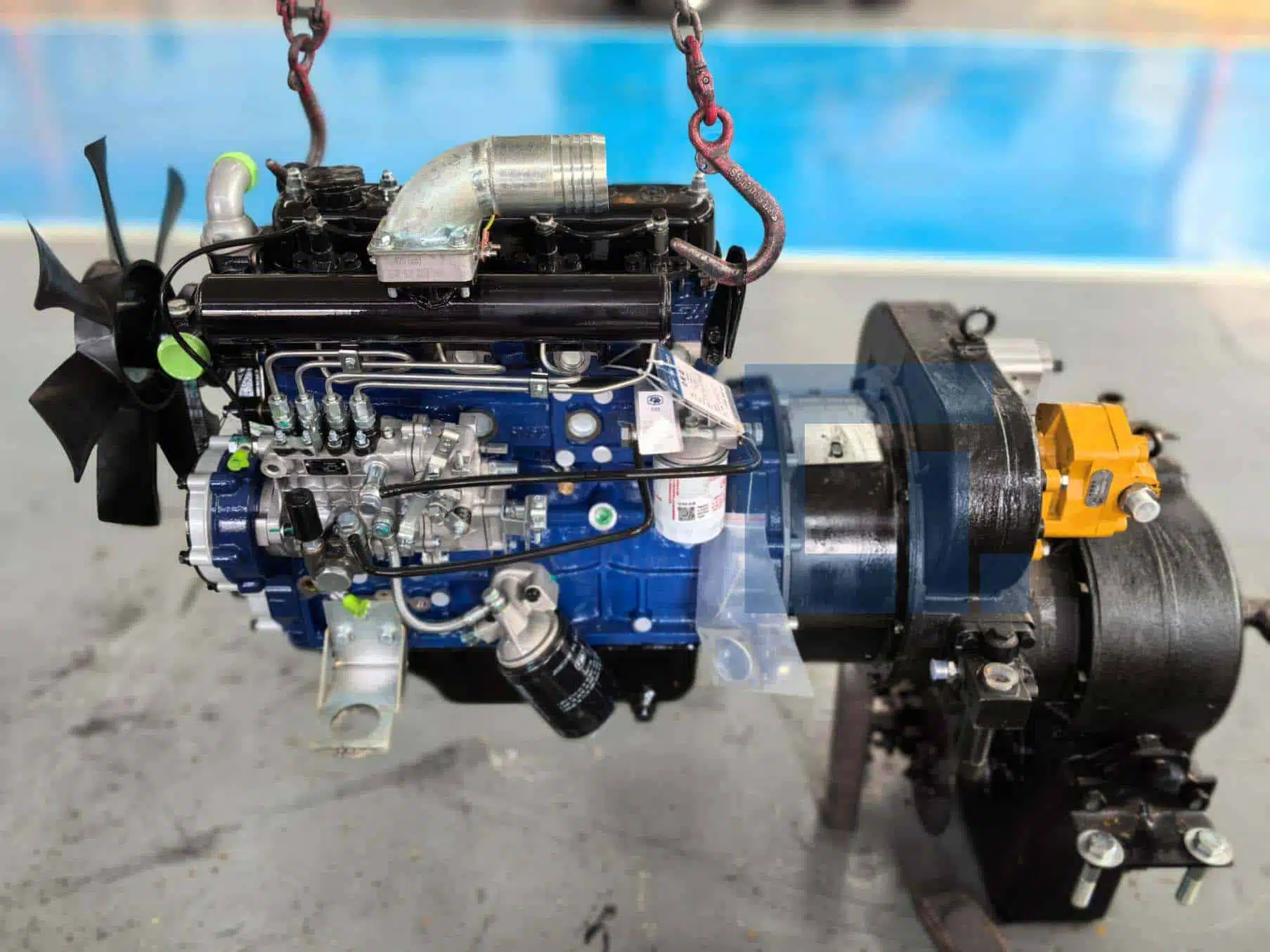 Engine and torque converter assembly of HIGHLAND HEAVY MACHINERY HILT 50 backhoe loader suspended in air, highlighting the optional hydrodynamic drive upgrade for improved torque and durability