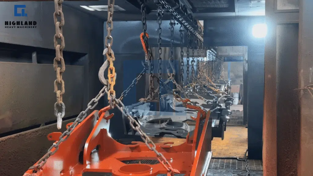 HIGHLAND HEAVY MACHINERY automated spray painting production line with a heavy-duty overhead chain conveyor transporting bright orange chassis frames through a brightly lit spray painting and baking tunnel.